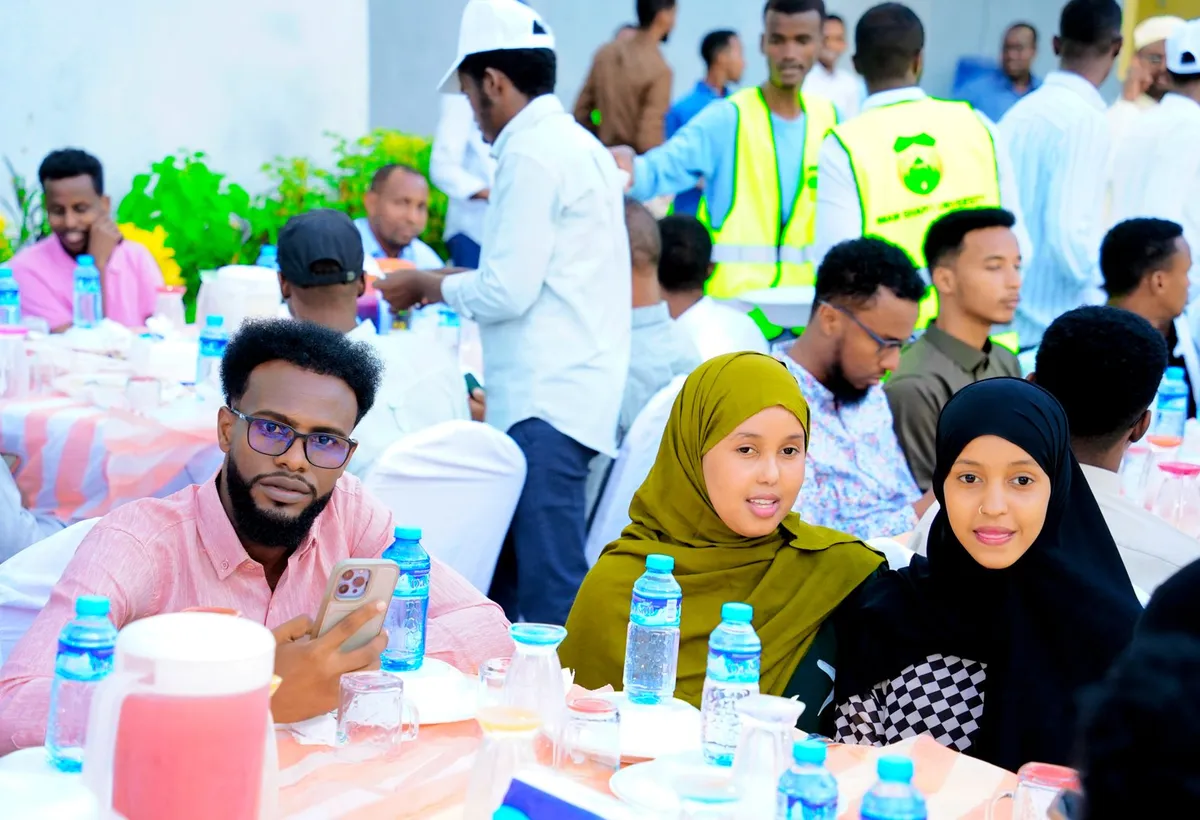 A large community gathering with participants seated at tables and volunteers assisting